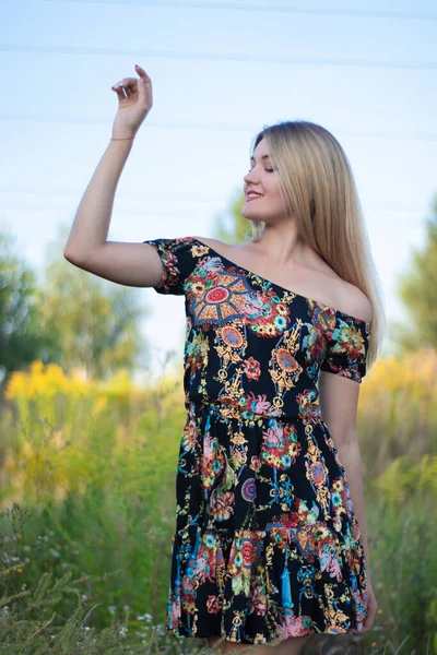 Overlight retrato brilhante de uma loira atraente encantadora em vestido florido no campo — Fotografia de Stock