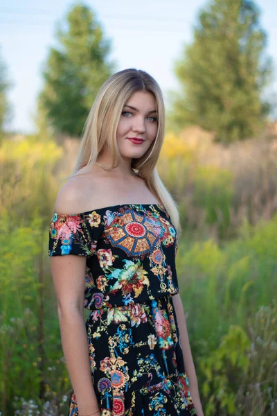 Overlight retrato brilhante de uma loira atraente encantadora em vestido florido no campo — Fotografia de Stock