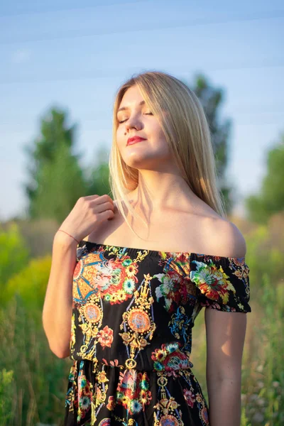 Overlight retrato brilhante de uma loira atraente encantadora em vestido florido no campo — Fotografia de Stock