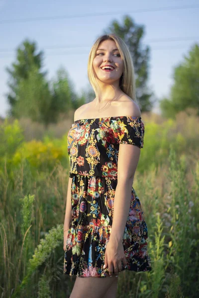 Overlight retrato brillante de una encantadora rubia atractiva en vestido de flores en el campo — Foto de Stock