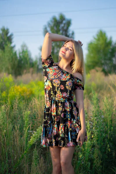 Açık renkli parlak bir portre. Tarlada çiçekli elbisesi olan çekici bir sarışın. — Stok fotoğraf