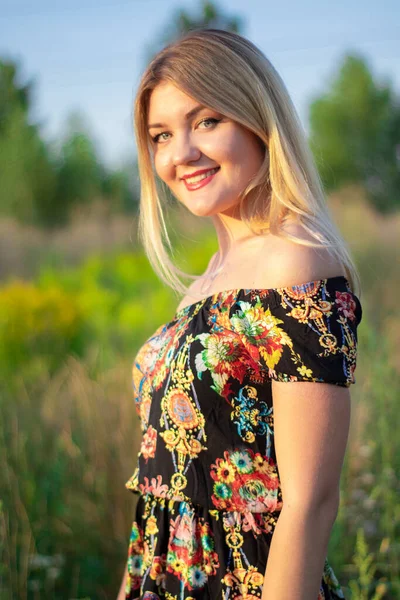 Overlight retrato brillante de una encantadora rubia atractiva en vestido de flores en el campo —  Fotos de Stock