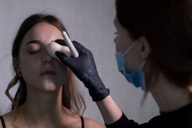 Tıbbi maske ve siyah eldiven ustası güzel esmerlere makyaj yapma süreci. güzellik ve kozmetik konsept