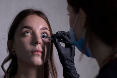 Tıbbi maske ve siyah eldiven ustası güzel esmerlere makyaj yapma süreci. güzellik ve kozmetik konsept