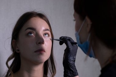 Tıbbi maske ve siyah eldiven ustası güzel esmerlere makyaj yapma süreci. güzellik ve kozmetik konsept