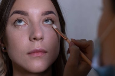 Tıbbi maskeli bir usta tarafından güzel bir esmere makyaj yapma süreci. güzellik, modellik ve kozmetik konsepti