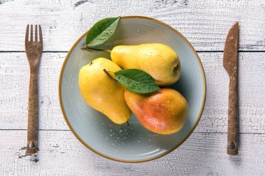 Çatal ve bıçak her iki tarafta sarı armut yaprakları yuvarlak mavi plaka ve eski kırık beyaz ahşap masa ile ıslak. Seçici odak. Yukarıdan görüntüleyin. Sağlıklı beslenme kavramı.