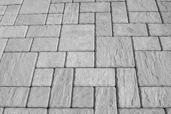 Geometric horizontal monochrome background with artificial stone paving made of square blocks of different shapes and sizes. Perpendicular and parallel lines. High angle view. Black and white image.