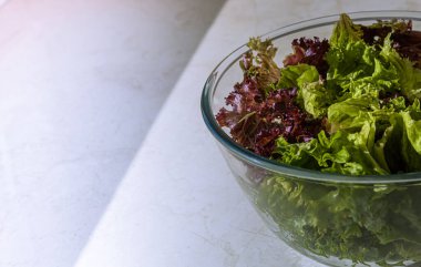 Büyük cam kase dolusu taze yeşil ve kırmızı marul yaprağı. Kase masa yüzeyinde. Seçici odaklanma. Sağlıklı beslenme ve beslenme konsepti. Büyük kopya alanına sahip yatay arkaplan.