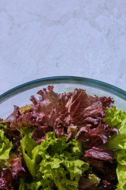 Büyük cam kase dolusu taze yeşil ve kırmızı marul yaprağı. Kase masa yüzeyinde. Seçici odaklanma. Sağlıklı beslenme ve beslenme konsepti. Büyük kopya alanı olan dikey arkaplan.