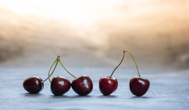 Olgun koyu kırmızı ve siyah kirazların yakın çekimi. Mavi ve altın yüzeyde üst üste beş tatlı kiraz. Kopya uzayı ile yatay arkaplan. Sağlıklı beslenme ve beslenme konsepti. Seçici odak.