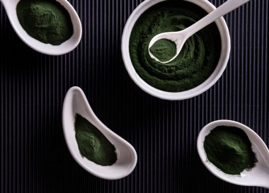Doğal yeşil klorella ya da dört farklı şekilli beyaz porselen kasede spirulina tozu. Sağlıklı süper yiyecekler ve diyet konsepti. Dikey çizgili siyah kağıt arkaplanı.