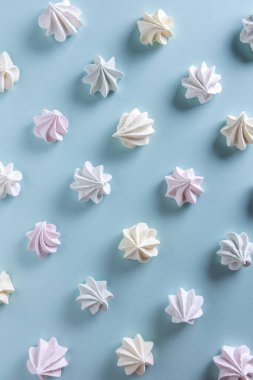 Açık yeşil, beyaz, sarı ve pembe kurabiyeli desenler. Kremalar mavi kağıt arkaplanda sıralanmış yatıyor. Sağlıksız gıda konsepti. Doğrudan görüş açısının üstünde. Dikey yönelim.  