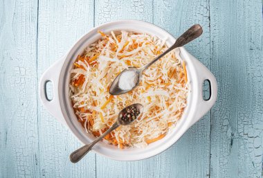 Ahşap masanda rendelenmiş lahana ve havuç dolu bir kap. İki metal kaşıkta tuz ve biber tavanın üzerinde sebzelerle birlikte. Mayalanmış lahana pişirme aşaması. Sağlıklı gıda konsepti için arka plan.