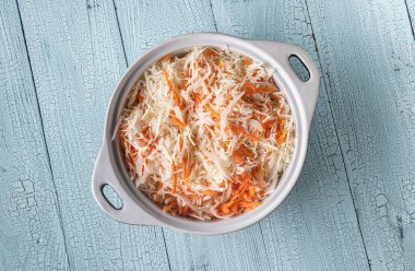 Rendelenmiş lahana dolu beyaz seramik tava ve tahtadan yapılmış ahşap mavi masa yüzeyinde havuç. Lahana salatası, mayalanmış lahana ve salata için aşçılık aşaması. Sağlıklı gıda konsepti için düz zemin.