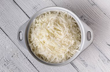 Tahtalardan yapılmış eski ahşap masa yüzeyinde rendelenmiş lahana dolu beyaz seramik tava. Lahana salatası, mayalanmış lahana ve salata için aşçılık aşaması. Sağlıklı gıda konsepti için düz zemin.