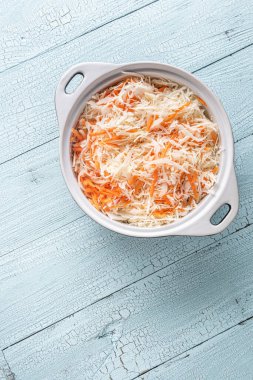 Beyaz seramik tepsi rendelenmiş lahana ve eski ahşap mavi masada havuç. Lahana salatası, mayalanmış lahana ve salata için aşçılık aşaması. Sağlıklı gıda konsepti için dikey arka plan. Boşluğu kopyala.