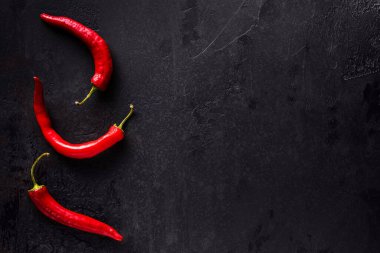 Üç kıvrımlı kırmızı kırmızı biber dokulu siyah taş yüzeyde. Baharatlı malzeme içeren yatay arkaplan ve metin için büyük kopya alanı. Sağlıklı gıda konsepti. Doğrudan yukarıdan görüntüle