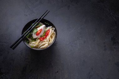 Baharatlı Asya çorbası tavuk buketi ve et, kırmızı biber, taze kişniş ve soğan, siyah yüzey üzerinde çubuklar olan siyah çorba kasesinde Japon eriştesi. Uzayı kopyala Yatay yönelim.