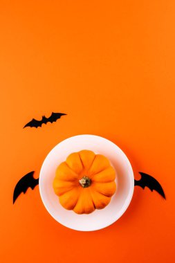 Uçan beyaz, siyah kanatlı, turuncu balkabağı ve dikey turuncu kağıt zemin üzerine oyulmuş siyah yarasa. Uzayı kopyala Düz yatıyordu. Cadılar Bayramı sembolleriyle komik bir görüntü.