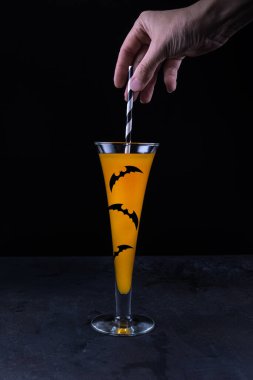 Kadın, kağıt kamışla bardağa alkolsüz moktail koyup kağıt yarasalarla süsleyip siyah desenli taş masa yüzeyinde duruyor. Cadılar Bayramı 'nda plastik sağlıklı yemek menüsü yok.