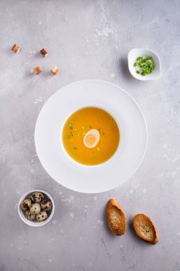 Beyaz çorba tabağında bulyon, doğranmış taze soğan veya soğan, bıldırcın yumurtası, kızarmış ekmek ve gri arka planda kızarmış ekmek. Düz yatıyordu. Dikey oryantasyon. Ev yapımı sağlıklı yeme ve diyet konsepti