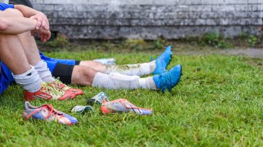 Futbolcular oyun yenilgisinden tarafından hayal kırıklığına uğramış bir futbol maçı sonrası çimenlerin üstünde oturuyorsun, futbol bot ve çim üzerinde başlık 16 x 9 biçimi dağınık Muhafızlar shin