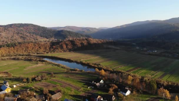 Vlotte vlucht over het oude dorp en de rivier in de vallei van de Karpaten, Oekraïne. Herfst tijd, luchtfoto — Stockvideo