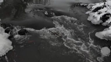 Nehrin akışı su, yakın çekim. Kar ve buz sarkıtları kıyısında. Ağır çekim