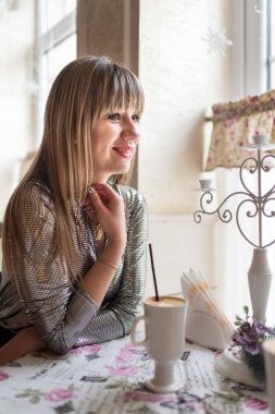 Güzel genç kadın rahat kafede masada oturur ve güzel kokulu latte sahiptir. Gülümseme ve yüzünde olumlu duygular.