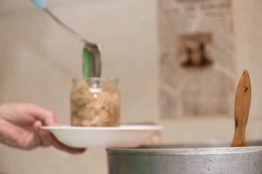 Cam bir kavanozu haşlanmış etle doldurmak. Evde domuz yahnisi pişirmek, yakın çekim işlemi. Tahta kaşık tavadan çıkıyor