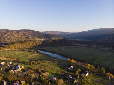 Karpat Dağları, Ukrayna. Gün batımında ormanlar ve nehir, çayırlar ve tepeler ile sonbahar dağlarının Havadan Drone Görünümü yumuşak ışık