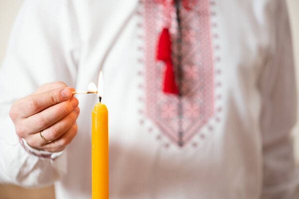 Ukrainian man in embroidered shirt lights a candle. Themes of celebrating Easter or Christmas, Day of memory of the victims of the Holodomor or the victims of the war