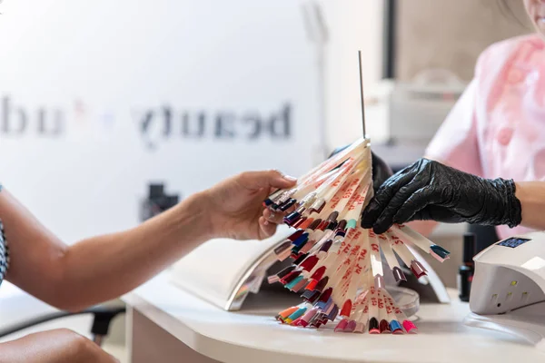 Profesjonalny kosmetolog pokazuje paletę kolorów manicure z lakierem żelowym, próbki. Zamknij proces. Kobieta w salonie piękności. Uroda i samoopieka — Zdjęcie stockowe