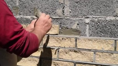 Adam dekoratif tuğlalarla duvarın ön cephesini süslüyor, manzarayı kapatıyor. Yapıların duvarlarını kaplamanın süreci