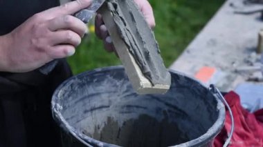 Adam kovadan tutkal alıyor ve dekoratif tuğlaya spatula sürüyor. Yapıların duvarlarını kaplamanın süreci
