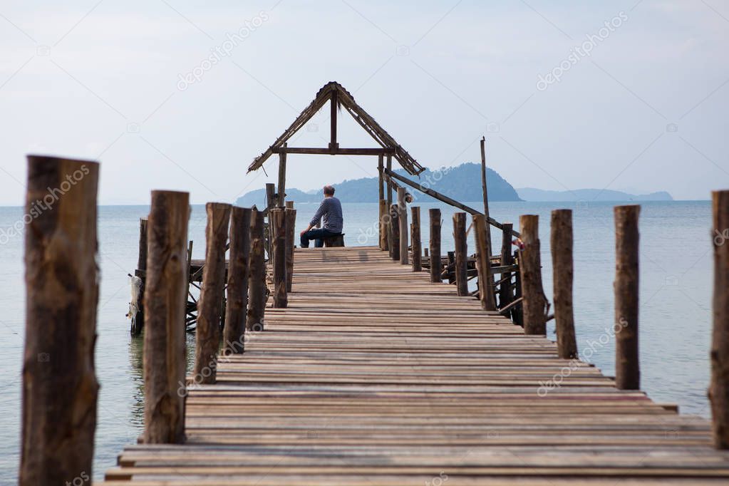 The old man sits on the pier and looks at the sea