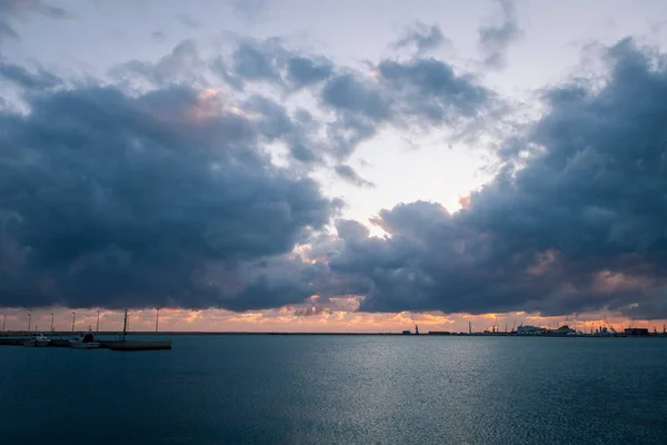 Nascer do sol sobre o mar com nuvens ameaçadoras no fundo do porto comercial — Fotografia de Stock