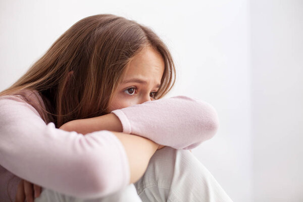 Young teenager girl with sad eyes sitting on the floor propping head on her knees - closeup portrait