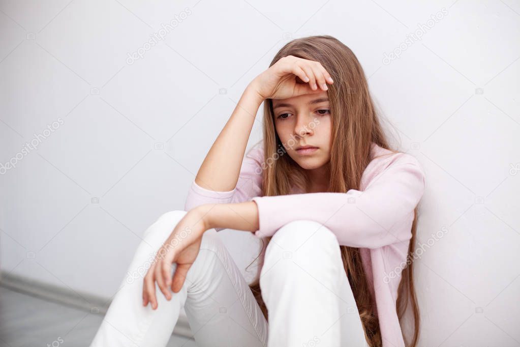 Young teenager girl having a heartache - sitting on the floor by the wall with a sad expression