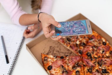 Bir smartphone kullanarak - bir kutu pizza, closeup çerçeveleme yemeğine bir fotoğraf çekici genç Genç kız