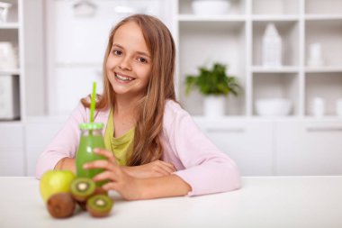 Mutlu genç kız geniş bir gülümseme ile masadan mutfağı - taze yeşil meyve suyu ile