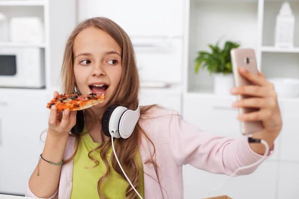 代の女の子を Selfie に最適なフレームをお探し キッチンでピザを食べて彼女のスマート フォンを使用して — ストック写真