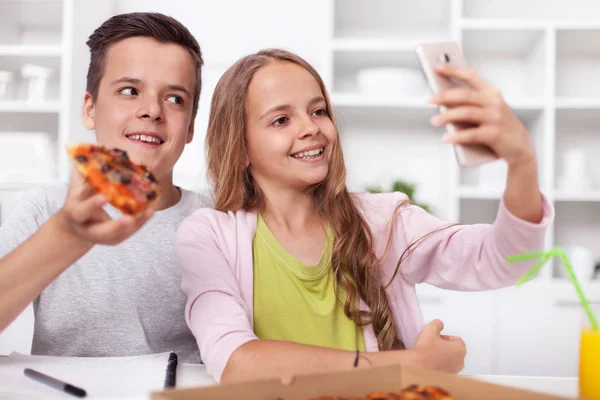 年轻的少年男孩和女孩在厨房里吃自拍的比萨饼 在他们的智能手机摄像头里微笑 — 图库照片