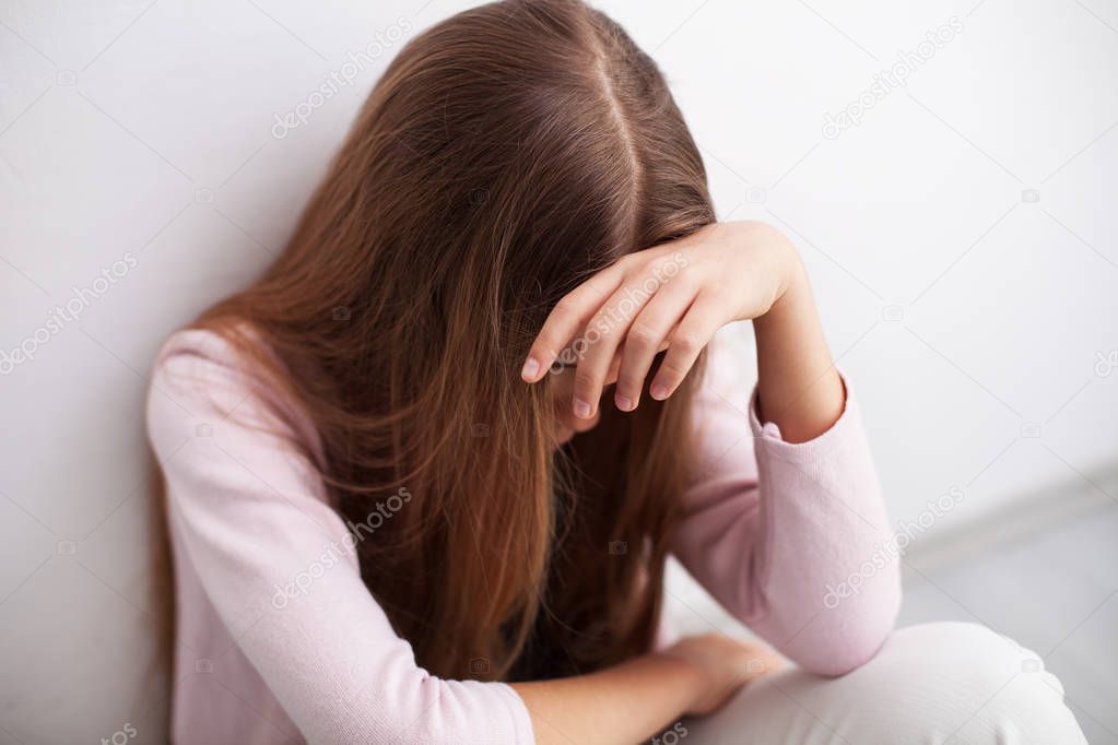 Depression in adolescence - young teenager girl sitting by the wall propping her head overwhelmed by problems