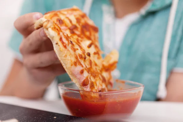 Рука занурює шматочок піци в томатний соус в миску — стокове фото