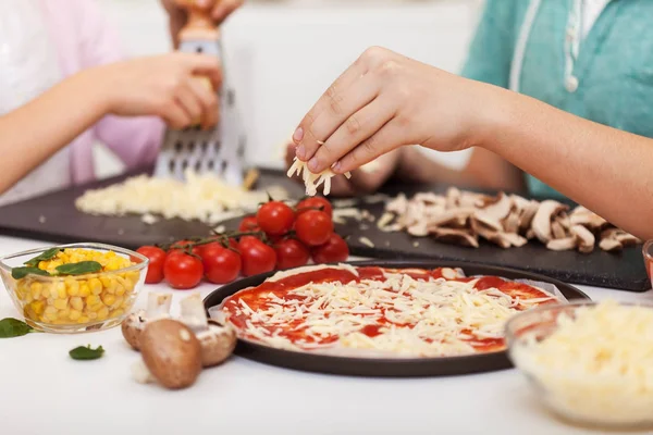 Jovens mãos preparam pizza em casa - ralar e polvilhar os queijos — Fotografia de Stock