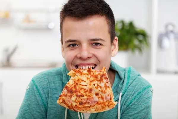 Ung pojke ha roligt att äta en pizza-med en skiva hängande från — Stockfoto