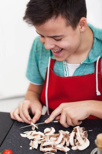 Junger glücklicher Junge bereitet in der Küche ein Gericht zu - Scheibe Pilz — Stockfoto