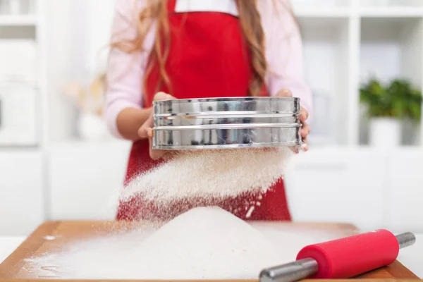 Girl sifting flour in the kitchen using a metallic sieve — Stock Photo, Image